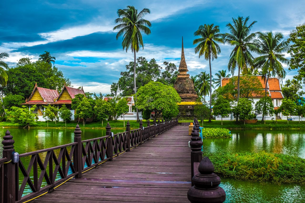 Explore the tranquil beauty of Sukhothai's temple surrounded by lush greenery and serene waters.